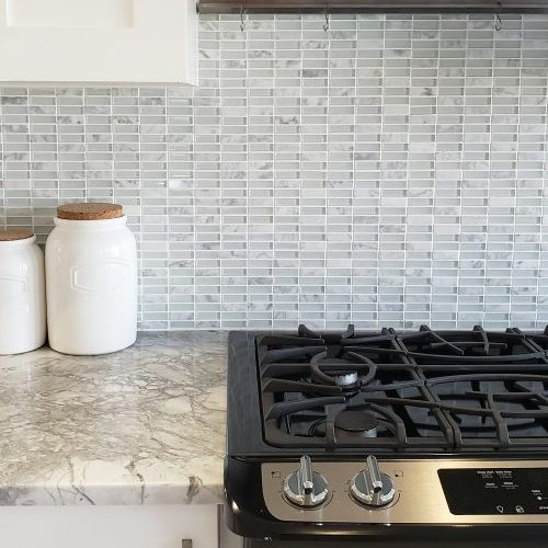 Modern kitchen design with gas stove appliance and clean white cabinets and mosaic tiles backsplash